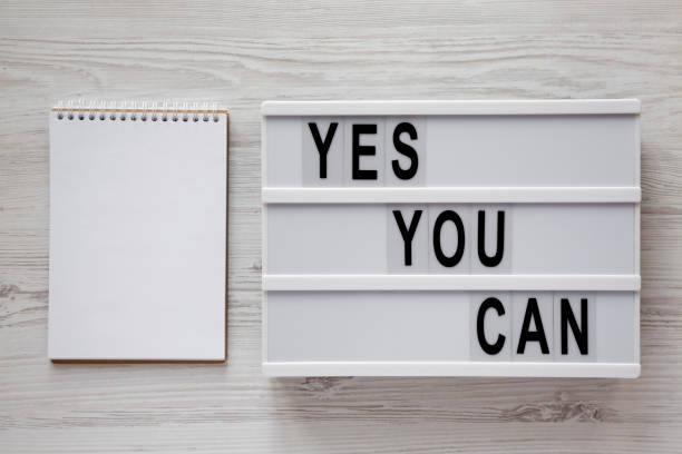 istock 'Yes you can' words on a modern board, blank notepad over white wooden background, top view. Overhead, from above. Flat lay. 1151733011