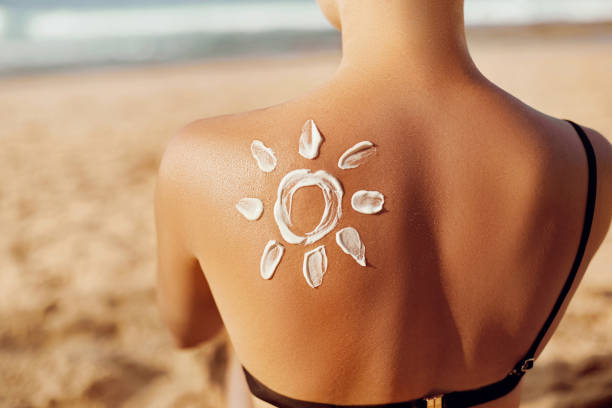皮膚護理。防曬。女人塗防曬霜。與陽光的婦女化妝水在海灘上的太陽. 女性的肖像與畫太陽在肩膀上。防曬霜。抱著保濕防曬霜的女孩。 - 防曬油 個照片及圖片檔