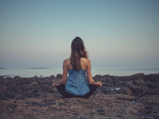istock Young woman meditating on coast at sunset 1151742104