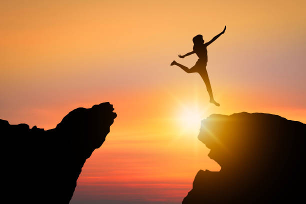 istock freedom and possible concept, silhouette people jumping over rock mountain successfully 1151745631