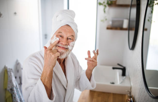 A senior man doing morning routine in bathroom indoors at home. A senior man doing morning routine in bathroom indoors at home, looking at camera. taking a bath photos stock pictures, royalty-free photos & images