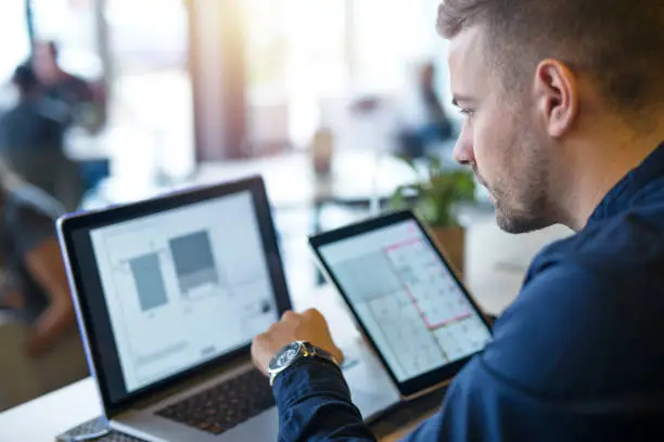 Photo of Business man looking and analyzing projects on his laptop computer and tablet.