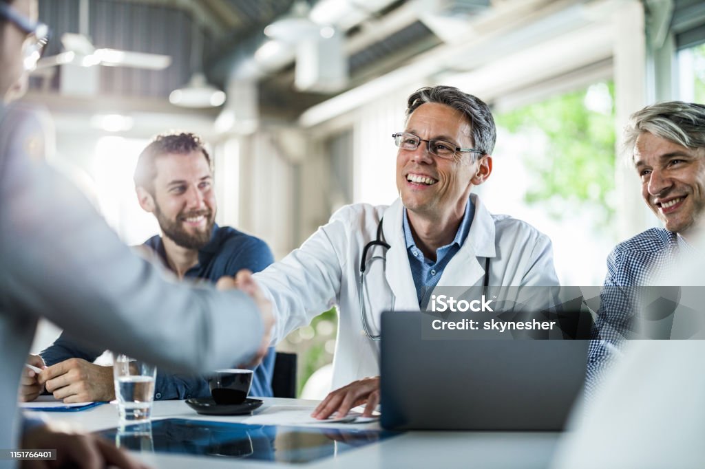 Glückliche Ärztin schüttelt Hände mit einem Geschäftsmann auf einem Treffen im Büro. - Lizenzfrei Arzt Stock-Foto