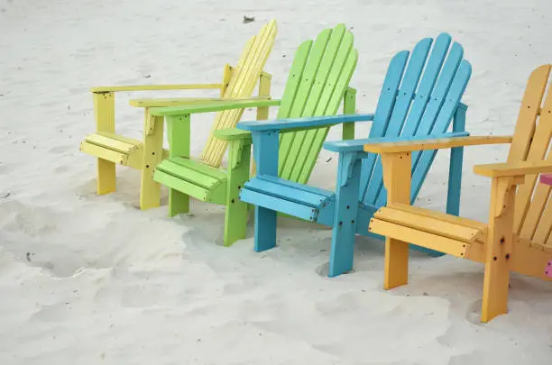 Bright pastel colored beach chairs on a white sand beach.