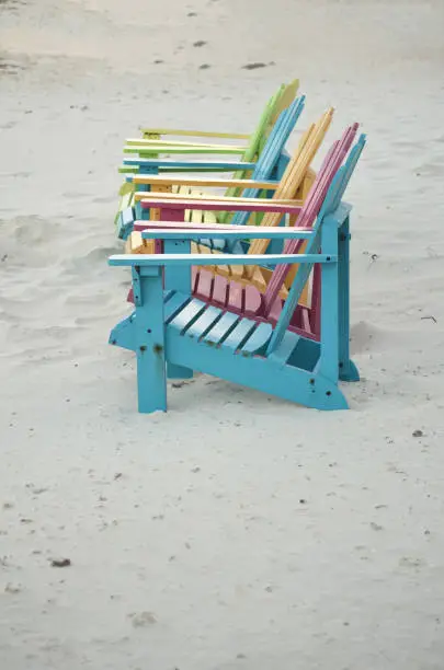 Pastel colored chairs with a white sandy beach.