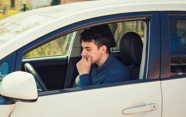 思慮深い若い男のドライバーは、彼の車の中で待っている心配そうに、あごの下に手を保持します。 - car driving inside of indoors ストックフォトと画像