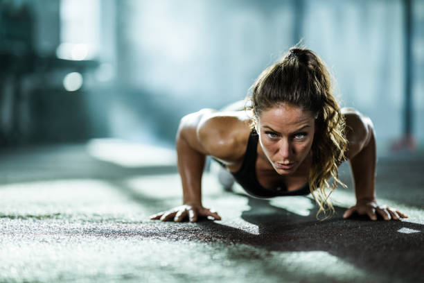 Athletic woman exercising push-ups in a health club. Young female athlete exercising push-ups with in a gym and looking at camera. Copy space. bodyweight training stock pictures, royalty-free photos & images