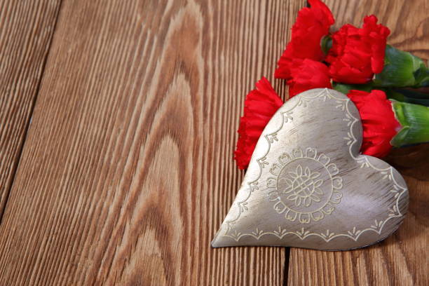 istock Heart shape decorated with fresh red carnations on an old brown board. 1151773610