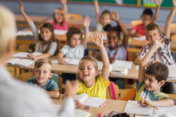 istock Large group of happy elementary students raising hands to answer the teacher's question on a class. 1151774645