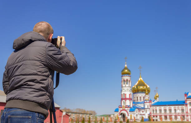 a photographer takes pictures of the church on camera with a tripod - reportage photographer photographing street imagens e fotografias de stock