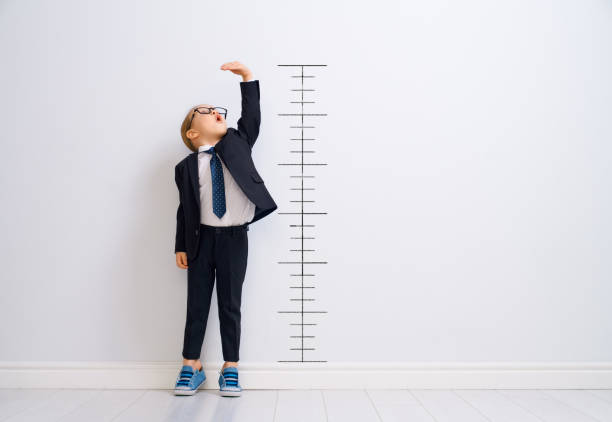 Kid is measuring the growth Little child is playing businessman. Kid is measuring the growth on the background of wall. Smart power concept. instrument of measurement stock pictures, royalty-free photos & images