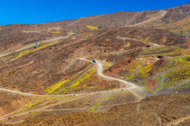 Photo of Scenic view of a mountain road with a bus moving to the top. Volcanic stone hills on The Mount Etna. Sicily, Italy