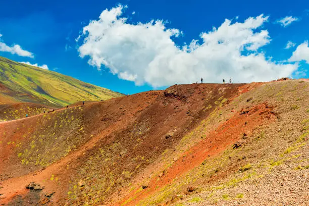 Beautiful colorful lava hills with group of people hiking to a volcanic crater. Mount Etna, Sicily, Italy.