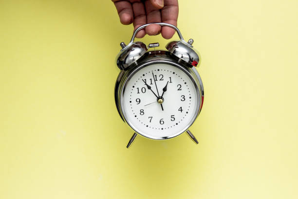 istock Metal alarm clock in hand isolated on yellow background. 1151781394
