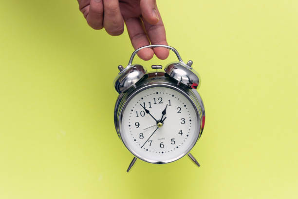 istock Metal alarm clock in hand isolated on yellow background. 1151781902