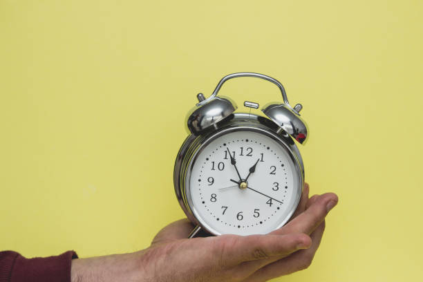 istock Metal alarm clock in hand isolated on yellow background. 1151781941
