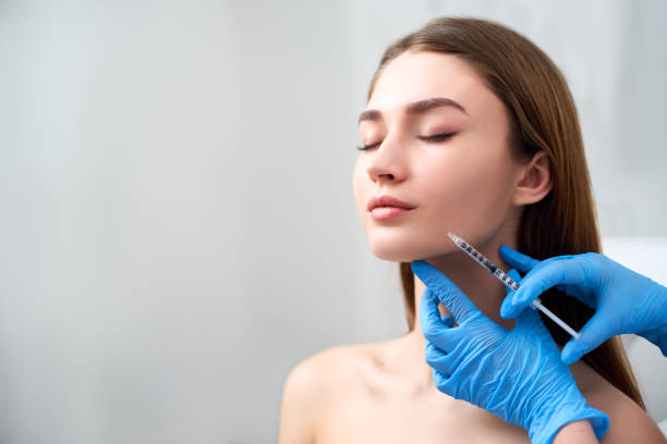 Smile lifting and lip augmentation. Beautician doctor hands doing beauty procedure to female face with syringe. Young woman's mouth countouring with filler injection. Marionette lines treatment stock photo