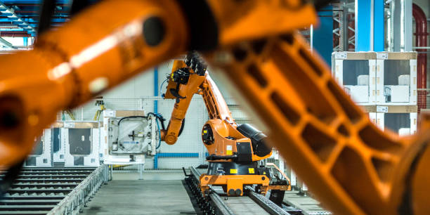 Photo of two robotic arms doing work in a factory assembly line Photo of two orange robotic arms moving washing machines on a factory assembly line. industrial orange stock pictures, royalty-free photos & images