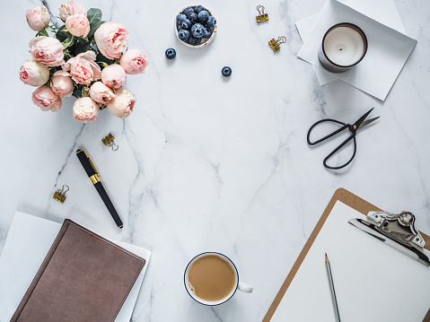 Top view of female home office with copy space in center. Clipboard, flowers, scented candle on white marble. Feminine home office mock up with copy space for text or design. Flat lay