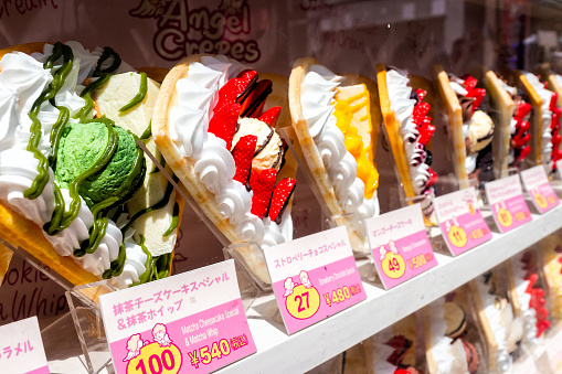 Tokyo, Japan - April 2, 2019: Takeshita street in Harajuku with display of colorful dessert crepes French pancakes in store with prices and signs