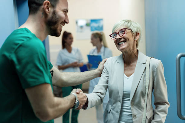 happy senior woman shaking hands with a surgeon at hospital hallway. - doctor patient greeting talking imagens e fotografias de stock