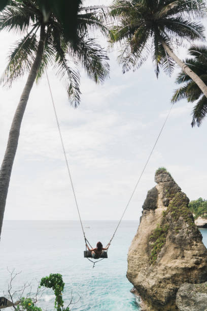 ヌサ・ヌサペニダの海の上のスイングの女性の風光明媚な景色 - nusa lembongan bali island beach ストックフォトと画像