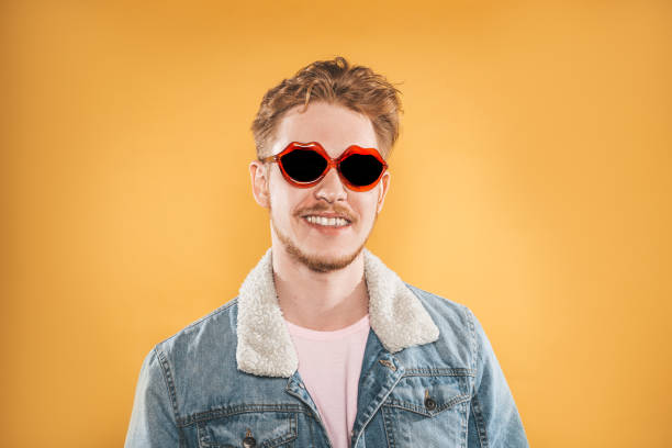 istock Smiling young man in lip shaped sunglasses on yellow background 1151794614