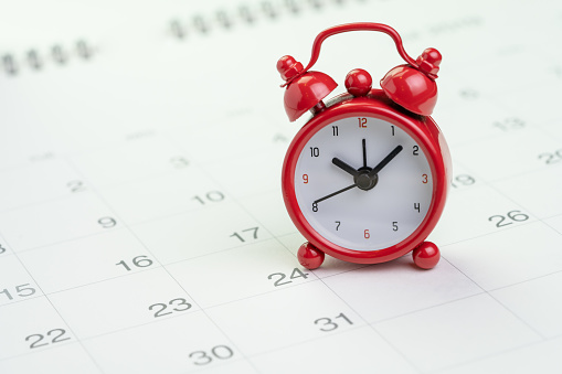 Recordatorio de fecha y hora o concepto de fecha límite, pequeño reloj de alarma rojo en el calendario blanco limpio con el número de días, contando hasta vacaciones, vacaciones o fin de mes photo
