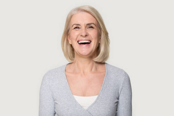 Headshot happy aged female laughing posing on grey studio background Head shot portrait overjoyed blond middle aged female smiling look at camera laughing feels happy pose isolated on grey studio background, advertise clinic procedure dental care prosthesis for seniors prosthetic equipment photos stock pictures, royalty-free photos & images