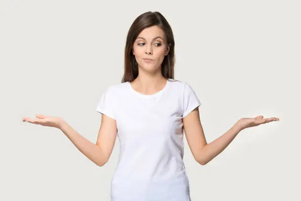 Photo of Millennial woman stretched hands thinking makes choice on grey background