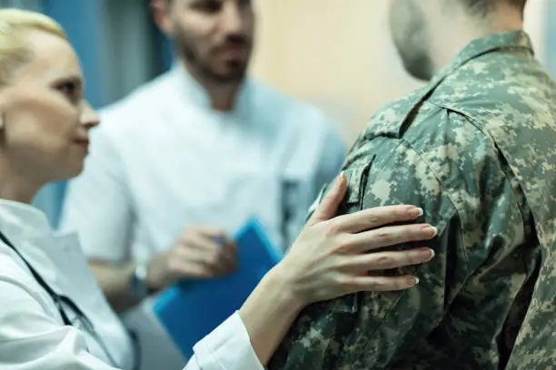 Close up of army soldier being consoled while talking with doctors at clinic.