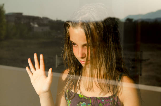 istock Anxious child with hand on window glass with reflection,looking sad and anxious 1151811663