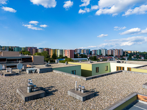 Aerial view of house flat roof on residental building. Modern architecture exterior. Air conditioning systems and ventilation structure. Residental building in background, sunny day.