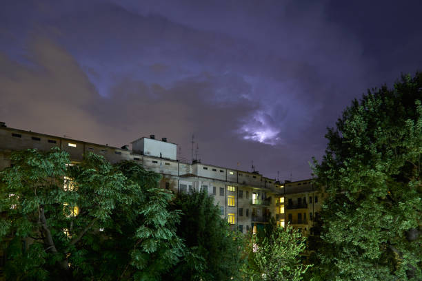 istock Buildings and green trees at night, illuminated sky during a lightning storm 1151826487