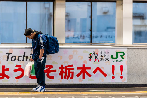платформа железнодорожного вокзала с молодым человеком, слушая музыку в ожидании синкансэна - high speed train audio стоковые фото и изображения