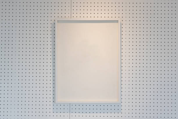 istock hanging empty wooden picture frame on orderly dot or hole wall with orange light form ceiling. 1151830979