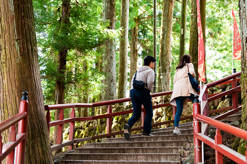 Nikko, Japan - April 4, 2019: Couple tourists walking on red railing stone steps stairs up in Tochigi prefecture in mountain forest leading to Toshogu shrine