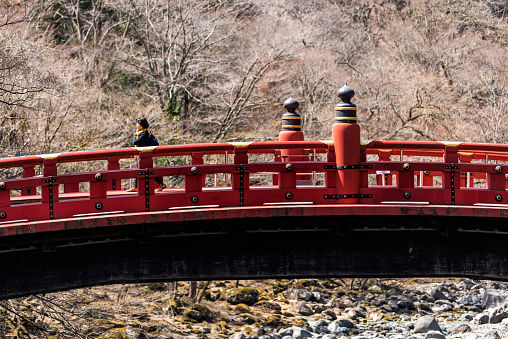 Nikko, Japan - April 4, 2019: Closeup of famous red bridge landmark in Tochigi prefecture in Japan with woman crossing in winter spring