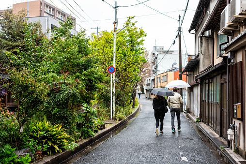 Kyoto, Japan - April 9, 2019: Takase river canal in residential neighborhood with green plants and people walking on street during rainy weather