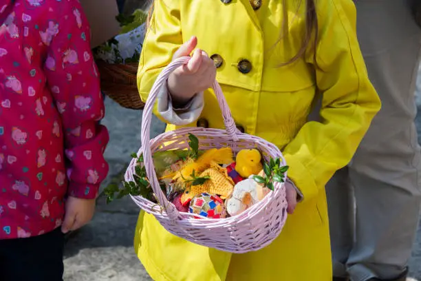 Children with their parents holding a traditional easter basket, a polish święconka, handmade decorations, eggs and prepared food. Happy children and easter celebration concept.
