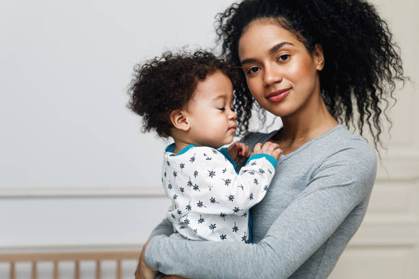 jeune maman retenant son petit garçon endormi. belle mère avec le fils dans le salon. - child offspring women posing photos et images de collection