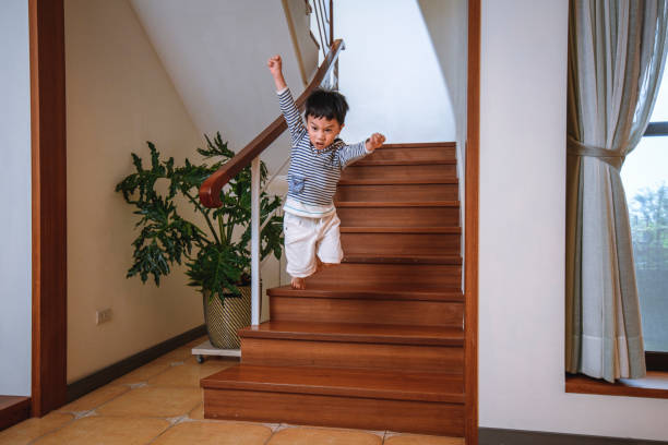 A cute toddler aged child walks up a wooden flight of stairs, wearing a yellow polka-dot skirt.  Her face is obscured by the composition.