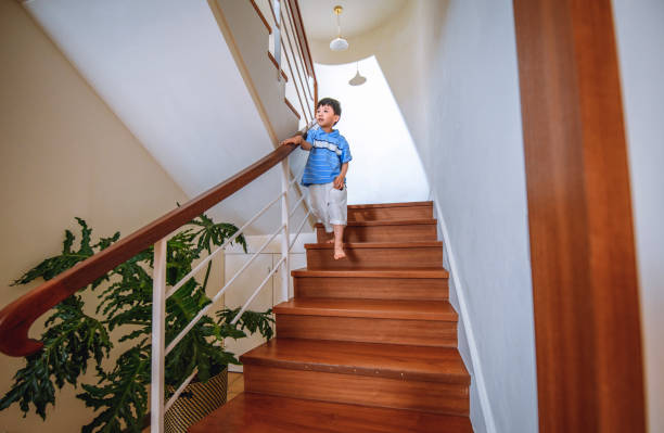 Young barefoot Taiwanese boy in casual clothing descending the staircase in a contemporary home interior.