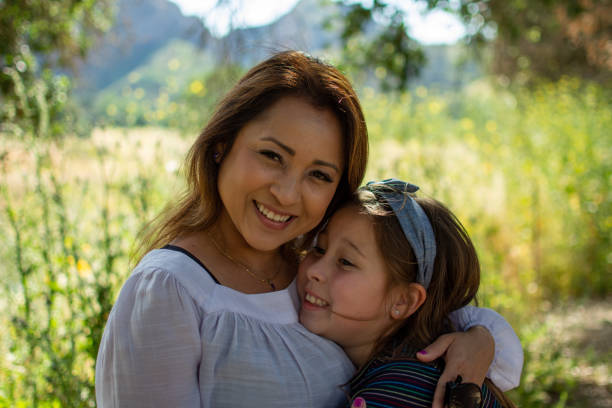 latina woman and daughter smiling together in front of a bright field at a park in the spring - spring happiness women latin american and hispanic ethnicity imagens e fotografias de stock