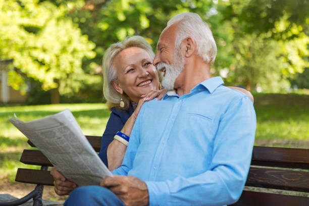 istock Senior couple relaxing outdoors reading newspaper in park sitting on a bench 1151851692