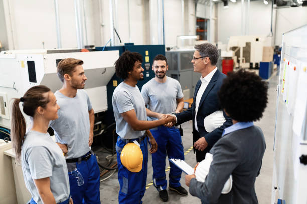 Happy corporate manager shaking hands with a worker while visiting a factory.