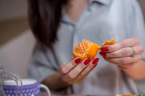 Woman peels tangerine sitting on the couch