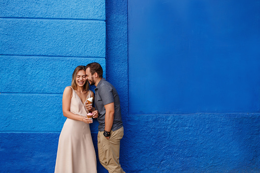 Happy couple in love eating ice cream and smiling against the blue wall