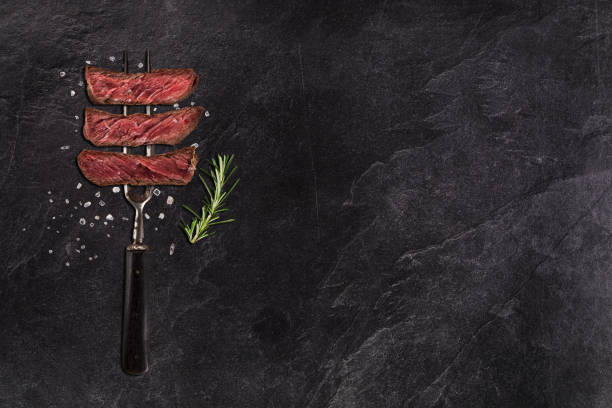 Sliced grilled beef steak with fork on black stone table Sliced grilled beef steak with fork on black stone table, top view carving set stock pictures, royalty-free photos & images