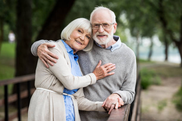 istock smiling senior couple hugging while standing by wooden bridge railing and looking at camera 1151872251